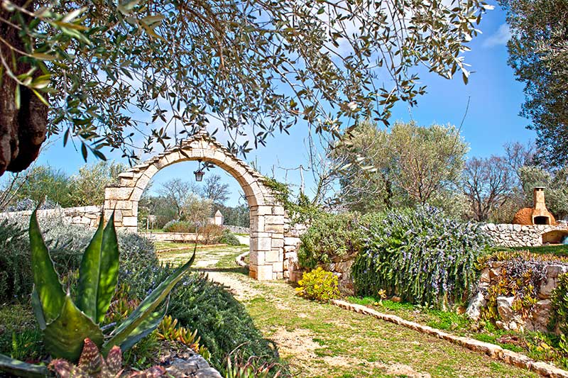 Portale in pietra tradizionale pugliese di ingesso al giardino con siepe di rosmarino